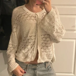 Vit stickad kofta från Indiska - Säljer en vit stickad kofta från Indiska i storlek L. Koftan har ett luftigt och snyggt hålmönster, knappar framtill och långa ärmar. Perfekt att slänga över en topp för en chill och trendig look.
