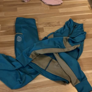 Blå byxor och och jacka  - Snygga blå träningsbyxor med beige paneler och en vit logga på benet. Byxorna har en slim passform och är gjorda i ett mjukt syntetmaterial som är perfekt för träning. Matchande jacka med dragkedja ingår om du vill ha ett komplett set.