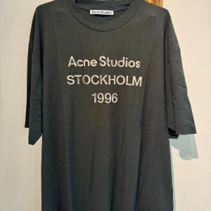 Svart Acne Studios t-shirt Stockholm 1996 unisex storlek M - Storlek M Unisex Svart t-shirt från Acne Studios med vit text 'Acne Studios STOCKHOLM 1996' på bröstet. Oversized passform, rund hals och tillverkad i mjuk bomull och hampa. Perfekt för en clean och stilren look.