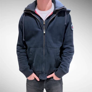 Mörkblå hoodie från Hollister  - Säljer denna asfeta hoodien från Hollister med dubbla dragkedjor. Den har också röd fordring inuti och i luvan vilket gör det snyggt med kontrasterna. Asfett plagg till hösten/våren. Eftersom det är dubbla dragkedjor är den lite extra isolerande och värmande 🙌