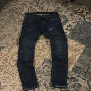 Lee Luke mörkblå skinny jeans - Mörkblå jeans från Lee, modell Luke, med skinny passform och klassisk femficksdesign. Jeansen har slitna detaljer på framsidan och kontrastsömmar. Materialet är jeans med en stretchig känsla för extra komfort.