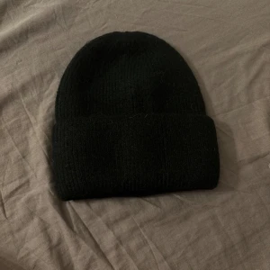Svart  mössa - Säljer en svart mössa med uppvikt kant. Enkel och stilren design som passar perfekt till kalla dagar. Mössan är mjuk och sitter skönt på huvudet, ett måste för vintern.
