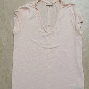 Blus - Säljer en ljusrosa blus med v-ringning och korta ärmar. Blusen har knappar längs hela ryggen som en snygg detalj. Tunt och luftigt material som passar perfekt till varmare dagar. Enkel och stilren design som är lätt att matcha.