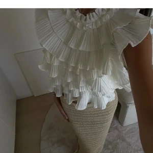 Vit Le Magda Blus - Superfin vit blus med volanger och hög hals. Toppen är ärmlös och har öppen rygg med knytband bak. Aldrig använd då de inte riktigt är min stil längre🥰