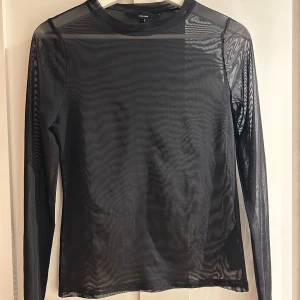 Svart mesh topp från Vero Moda - Säljer en svart mesh topp från Vero Moda i storlek S. Toppen är helt genomskinlig, har rund halsringning och långa ärmar. Perfekt att styla lager på lager för en cool look.