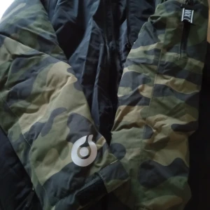 Vinter jacka - Säljer en snygg vindjacka från Woxd 720° i storlek 158. Jackan har coola camouflage-mönstrade ärmar i grönt och svart, med svart kropp och dragkedja framtill. Materialet är slitstark polyester och jackan har praktiska detaljer som kardborre vid ärmslut och märkta zip-pullers.