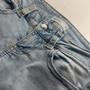 Ljusblå jeans  från Gina - Säljer ett par ljusblå jeans  från ginatricot med klassisk femficksdesign, knapp- och dragkedjestängning samt bälteshällor. Snyggt slitna detaljer och mjuk bomullskänsla. Perfekta för en avslappnad stil.