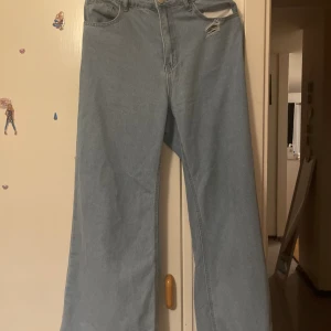 Ljusblå wide jeans med slitning - Säljer ett par ljusblå jeans med breda ben och hög midja. De har en snygg slitning vid fickan som ger en cool vibe. Den är oanvänt 