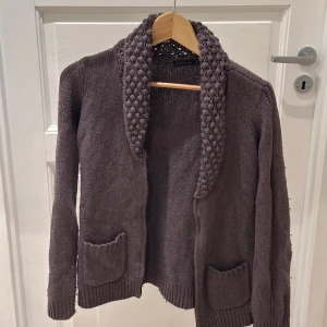 Brun stickad kofta från Stockh LM - Mysig brun stickad kofta från Stockh LM med grovstickad krage, två framfickor och dragkedja. Perfekt för lager-på-lager och har långa ärmar samt ribbade muddar. Snyggt avslappnad passform och passar dig som gillar klassisk stil.