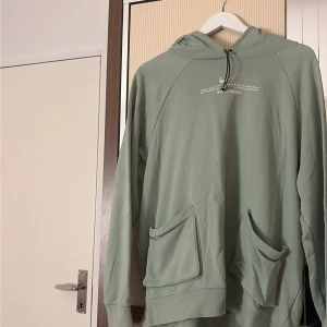 Grön hoodie från Nike med snörning - Snygg ljusgrön hoodie från Nike med tryck och Swoosh-logga på bröstet. Tröjan har huva med snörning, två stora fickor framtill och är tillverkad i mjuk bomullsmix. Perfekt för chill eller träning, loose fit och långärmad design.