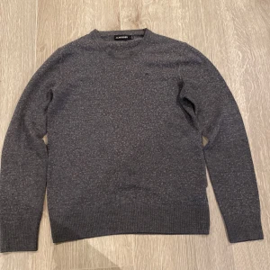 Mörkgrå stickad tröja J.Lindeberg L - Mörkgrå stickad tröja från J.Lindeberg i storlek Small Tröjan har rund halsringning, diskret broderad logga på bröstet och ribbade muddar vid ärmslut och nederkant. Perfekt för lager-på-lager under höst och vinter.