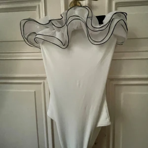 Vit body med volang - Säljer min super snygga vita body som har volanger med svart kant! Den är så bekväm och såå snygg!! Kör nu lag postar snabbt!!💗💗💗