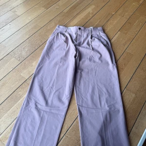 Ljuslila kostymbyxor med raka ben - Snygga ljuslila kostymbyxor med raka ben och hög midja. Byxorna har pressveck fram, sidofickor och bakfickor med knapp. Perfekt för dig som gillar stilrena och trendiga plagg i en soft färg. Materialet känns som bomull eller polyester.