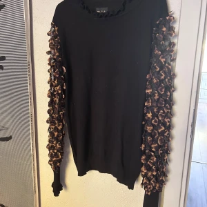 Svart tröja med leopardärmar  - Cool svart tröja från Chica London med unika långärmade leopardmönstrade detaljer. Ärmarna är transparenta och 3D-effekt med små tygbitar i leopardmönster. Perfekt för dig som vill sticka ut med en trendig och edgy look. Fin rundad hals. Material finstickad bomull och elastane.  Strl Large men mer som en M