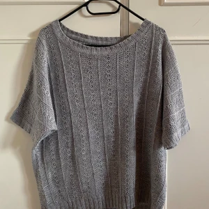 Grå stickad kortärmad tröja - Snygg grå stickad tröja med korta ärmar och rund hals. Tröjan har ett diskret hålmönster framtill och ribbade kanter vid hals, ärmslut och nederkant. Perfekt för lager-på-lager och chill stil under vår och höst. Har aldrig använt för den passar ej men den passar även till en s person 