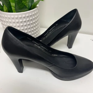 Svarta pumps från Dasia i skinn mer som 38 i storlek  - Snygga svarta pumps från Dasia i mjukt skinn med rund tå och hög klack. Klassisk och stilren modell med svart innersula och diskret söm längs kanten. Yttersulan har mönstrad gummisula för extra grepp. Perfekt för dig som gillar enkel och elegant stil.