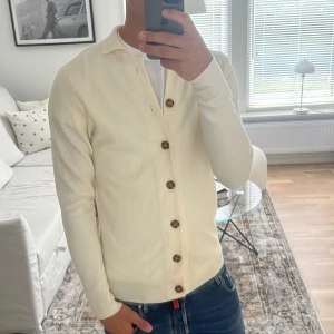 John Henric stickad cardigan merinoull  - As fet stickad cardigan, ljus färg, perfekt till lite kallare dagar då man vill ha olika lager. Skick 8/10 några små defekter men kan nog försvinna enkelt annars sitter den riktigt skönt. Hör av vid funderingar!
