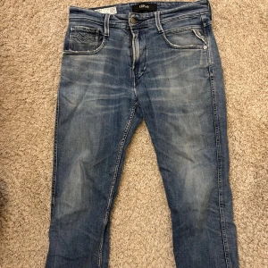 Replay Anbass slim jeans blå 29/32 - Snygga Replay Anbass jeans i slim fit med klassisk femficksdesign och ljusblå tvätt. Jeansen har diskreta slitningar och kontrastsömmar, tillverkade i mjukt jeanstyg som sitter skönt. Perfekt för dig som gillar en smalare passform och stilren look.