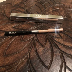CAIA Duo Eye Pencil Holiday Glam - Snygg duo ögonpenna från CAIA i Holiday Glam Edition. Ena sidan är svart eyeliner och andra sidan är beige kajal, perfekt för att skapa kontrast och öppna upp blicken. Pennan har en stilren design med metallisk detalj i mitten.