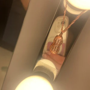 Halsband med jordnötsberlock  - Halspand i roséguld med en jordnötsformad berlock. Inte använd! Nypris 99kr