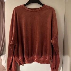 Rostbrun velourtröja från hunkmöller L - Mjuk och chill rostbrun långärmad tröja från H&M i storlek L. Tröjan är gjord i skön velour med loose passform och har rund halsringning samt breda muddar vid ärmslut och nederkant. Perfekt för dig som gillar comfy vibes och snygg färg.