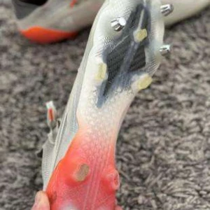 Beige fotbollsskor från Adidas - Snygga beige fotbollsskor från Adidas med silvriga ränder på sidan och orange detalj vid hälen. Skorna har snörning och är tillverkade i syntetmaterial med mesh för bra ventilation. Perfekta för dig som vill sticka ut på planen.