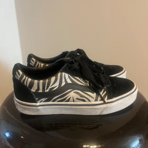 Vans sneakers med zebramönster - Ett par Vans sneakers med svart och vitt zebramönster i storlek 37! Skorna har klassisk låg modell, svarta snören och vit sula. Dem har använda fåtal gånger och är i bra skick!