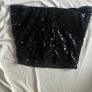 Svart glittrig paljett tubtopp - Säljer en svart minikjol täckt med glittriga paljetter som ger en riktigt festlig vibe. Funkar lika bra att ha som festtopp!Perfekt för dig som vill sticka ut på nästa fest eller event!