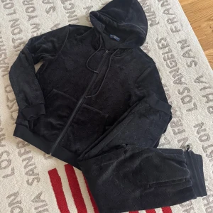 Svart velour hoodie från Louis Vuitton - Säljer en svart hoodie från Louis Vuitton i mjuk velour med monogrammönster över hela plagget. Tröjan har huva med snörning, dragkedja framtill och långa ärmar. Perfekt för dig som vill ha en lyxig och bekväm streetstyle-look.