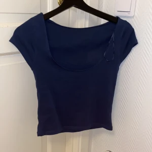 Mörkblå croppad topp med rund hals - Snygg mörkblå croppad topp med rundad halsringning och korta ärmar. Toppens material är mjuk och stretchig bomull, vilket gör den bekväm och enkel att bära. Perfekt att styla med jeans eller kjol för en chill look.