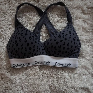 Leopardmönstrad topp från Calvin Klein - Snygg mörkgrå leopardmönstrad topp från Calvin Klein med bred vit resår och logga. Toppen har korsade axelband. 