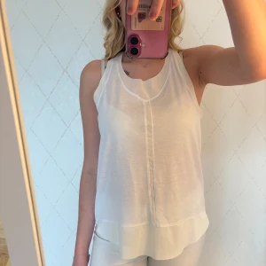 Vitt träningslinne från Adidas - Säljer en vit, luftigt träningslinne från Adidas med brottarrygg och v-ringning. Toppen är ärmlös och har en lätt transparent känsla med en snygg söm framtill. Perfekt för varma dagar eller träning. Adidas-logga i nacken.