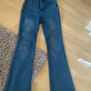 Blå bootcut jeans med hög midja - Snygga blå jeans med bootcut passform och hög midja. Klassisk femficksdesign och knappstängning fram. Jeansen har en lätt tvättad look och är tillverkade i jeansmaterial som känns slitstarkt och bekvämt. Perfekt för dig som gillar retrovibbar och vill ha ett coolt snitt.aldrih använt och köpte för 300 men säljer för 200 kr. 