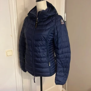 Mörkblå dunjacka från Parajumpers,S - Supersnygg mörkblå dunjacka från Parajumpers i storlek S. Jackan har huva, två dragkedjeförsedda fickor och coolt PJS-märke på ärmen. Lättviktig och quiltad design med hel dragkedja framtill, perfekt för kyliga dagar. 