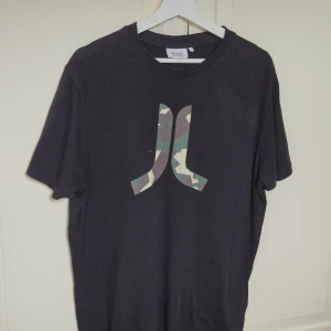 Svart vintage t-shirt från WESC med camologga L - Svart vintage t-shirt från WESC i storlek L med klassisk rund hals och korta ärmar. Framtill finns en stor logga i camouflage-mönster som ger en cool streetkänsla. Tillverkad i mjuk bomull för skön passform.