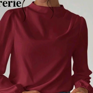 Vinröd blus med lång ärm burgendy  - Säljer en stilren vinröd blus med lång ärm och hög hals. Blusen har en mjuk, lätt glansig yta och ett snyggt nyckelhålsöppning bak i nacken. Ärmarna är lätt puffade och avslutas med resår vid handlederna. Perfekt till jeans eller kjol.