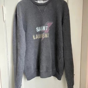 Saint Laurent sweatshirt Bolt - Grå sweatshirt från YSL Saint Laurent med ”Bolt” blixt- och logotryck på bröstet. Storlek: M men sitter mer som S. (Jag är 176 och den sitter rätt bra på mig.)