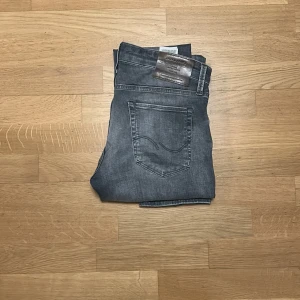 Jack & Jones jeans  - Slim/Glenn jeans från Jack & Jones i snygg grå tvätt med klassisk femficksdesign. Jeansen har en smal passform och raka ben, med diskreta slitningar och detaljerade sömmar på bakfickan. Perfekt för dig som gillar en modern och stilren look.