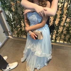 Ljusblå prinsess balklänning - Har bara använt en gång! Rekommenderar att ha en underkjol under klänningen så den är mer puffig och prinsesslik (man ska ha en underkjol), på bilderna hade jag inte en underkjol då min underkjol inte kom i tid till balen😕 Den är även för stor för mig vid brösten för jag har inte stora bröst alls. Klänningen försig är jätte fin, har pads så man behöver inte ha BH på sig. Där bakom är det som ett korsettsystem