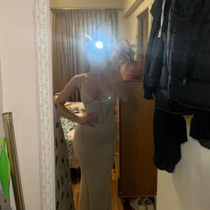 Beige stickad långklänning med snörning - Säljer en beige stickad långklänning med smala axelband och djup urringning. Klänningen har öppen rygg med snygg snörning och är figurnära med virkade detaljer. Perfekt för sommardagar och semester.