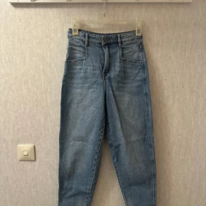 Blå denimjeans från Kappahl strl 34 - Snygga blå jeans från kappahl i  storlek 34. Modellen har hög midja, raka ben och klassiska fem fickor. Jeansen är tillverkade i hållbar bomullsdenim och har en cool vintagekänsla med ljus tvätt.
