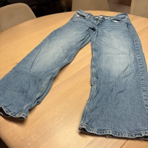 Wide leg jeans från H&M, ljusblå - Säljer ett par ljusblå wide leg jeans från H&M i storlek 164. Modellen har låg midja och justerbar midja, klassisk femficksdesign och slitningar för en chill vibe. Perfekt för dig som gillar loose fit och retro känsla.