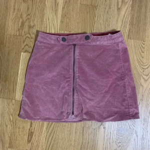 Rosa kjol med dragkedja - Kort mjuk rosa kjol med dragkedja framtill och två dekorativa knappar i midjan