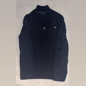 Svart half zip tröja Gant - Svart långärmad tröja från Gant med half zip och logga på bröstet. Perfekt för dig som gillar stilren och enkel design. Storlek L.