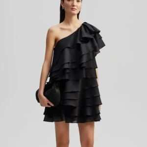 Svart oneshoulder volangklänning - Säljer en svart kortklänning med oneshoulder och flera lager volanger. Klänningen har en asymmetrisk axel och är tillverkad i ett lätt, flödande material som ger en snygg siluett. Perfekt för dig som gillar att sticka ut med stilrena detaljer.