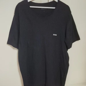 Svart t-shirt från BOSS i XL - Svart t-shirt från BOSS med enkel design och liten vit logotyp på bröstet. Rund halsringning och korta ärmar. Tillverkad i mjuk bomull som känns skön mot huden. Perfekt för dig som gillar stilrena och klassiska plagg. Knappt använd.