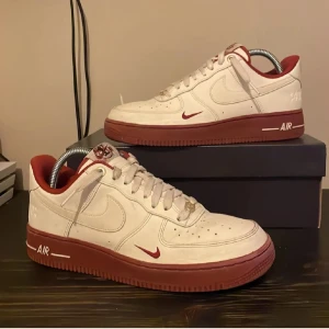 Nike Air Force 1 40th Anniversary vit/röd - Nike Air Force 1 40th Anniversary sneakers i vitt skinn med röda detaljer och röd sula. Låg modell med klassisk snörning, perforerad tå och broderad Nike Air-logga på hälen. Insida i rött tyg och liten röd swoosh på sidan. Perfekt för dig som gillar unika sneakers. Nypris 2000 kr mitt pris 450