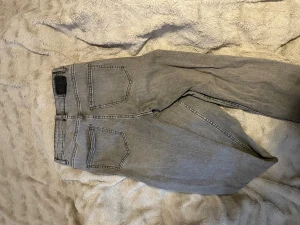 Grå jeans utsvängda jeans med slit från 157 - Snygga grå jeans från 157 med klassisk femficksdesign och raka ben. Jeansen har hög midja och är tillverkade i mjukt denimtyg som ger en skön känsla. Perfekt för dig som gillar en clean och enkel look.