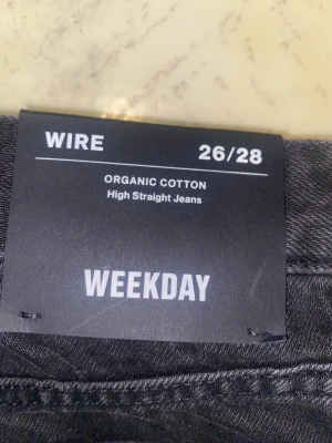 Svarta Weekday Wire High Straight Jeans - Svarta jeans från Weekday, modell Wire High Straight. Tillverkade i 100% ekologisk bomull med klassisk femficksdesign och raka ben. Hög midja och stilren look som passar till sneakers eller boots. Snyggt svart tyg och diskreta sömmar.