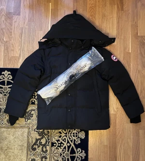 Ny Canada Goose Wyndhamn Jacka  - Helt ny och oanvänd Canada Goose Wyndhamn i svart med den ikoniska röda badgen. Jackan har fin, mjuk päls och är perfekt för kalla vinterdagar med både stil och funktion. Storlek [ Size M ]. Kan skickas på samma dag. Pris kan diskuteras. 